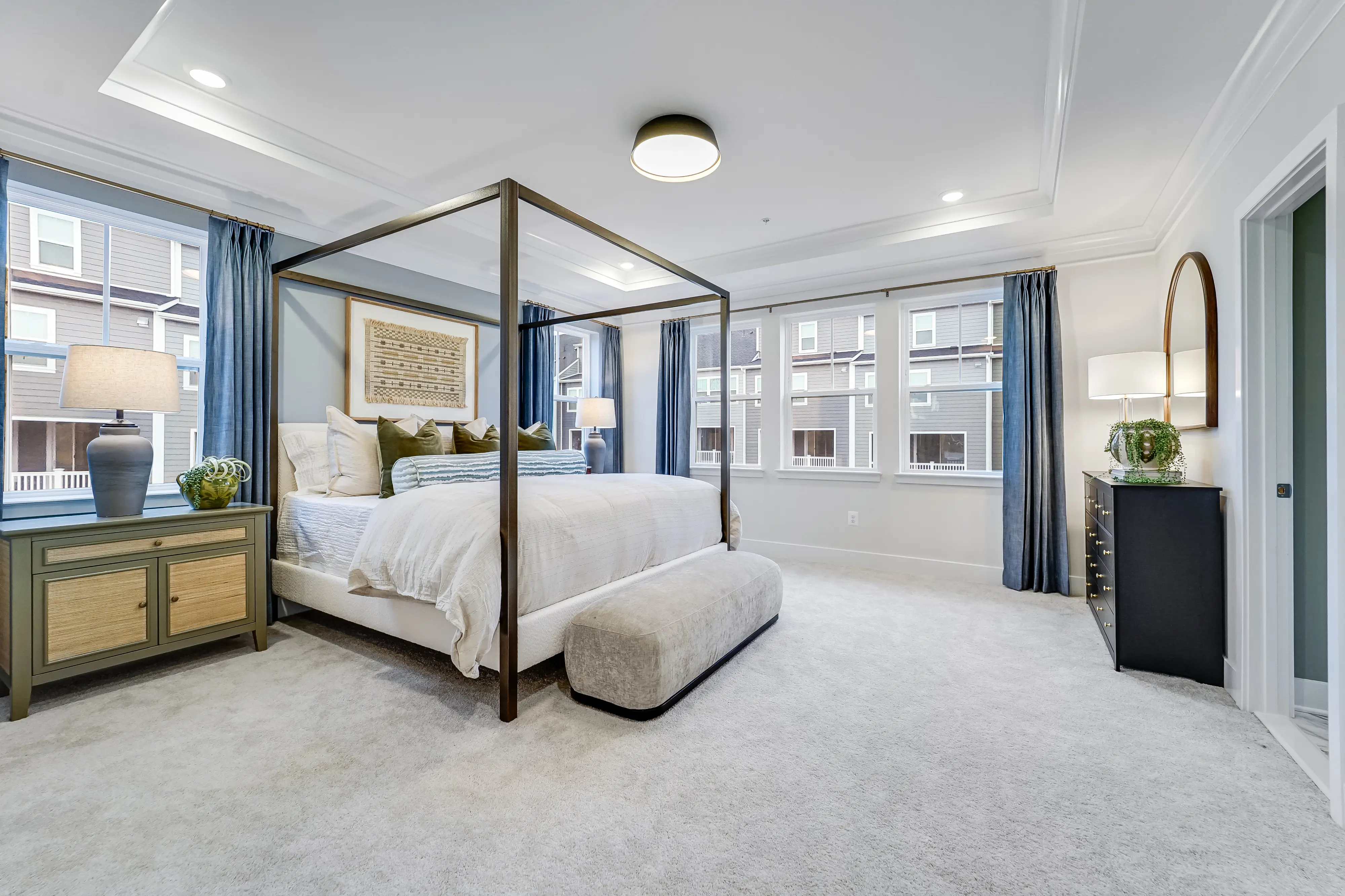Luxury furniture like a canopy bed and arched mirror inside a bedroom with new white carpets and plenty of natural light