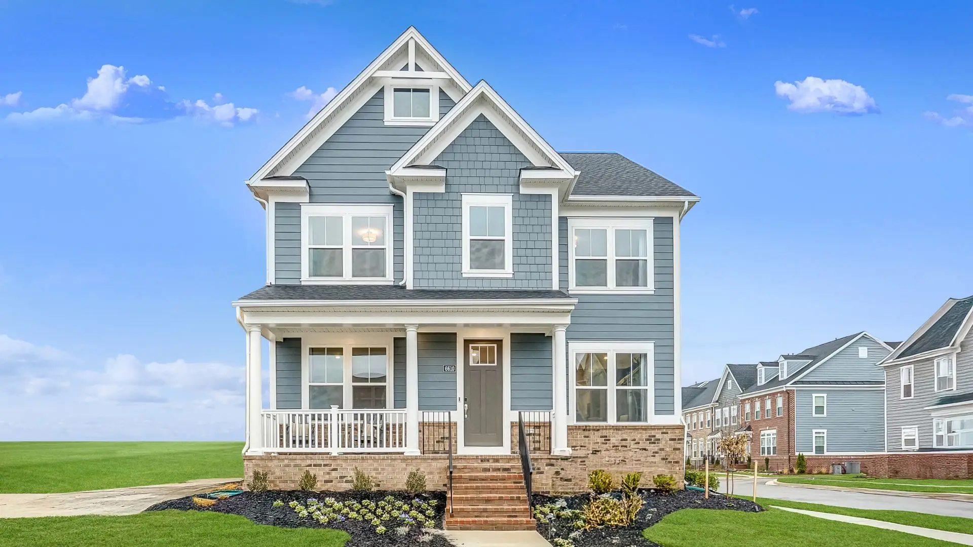 The exterior of a blue Lennar Home at Greenleigh in Baltimore County underneath a blue sky with other houses off in the distance and a green field next door