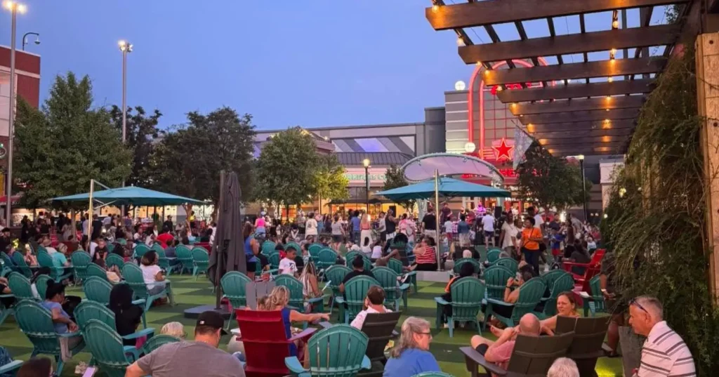 A crowd sitting in green chairs watching a concert at the Avenue at White Marsh MD at dusk